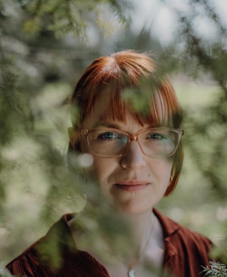 Karoline Krey, Coachin für persönliche Transformation bei marvelousme, Blick durch grüne Äste in die Kamera, ruhiges Naturporträt