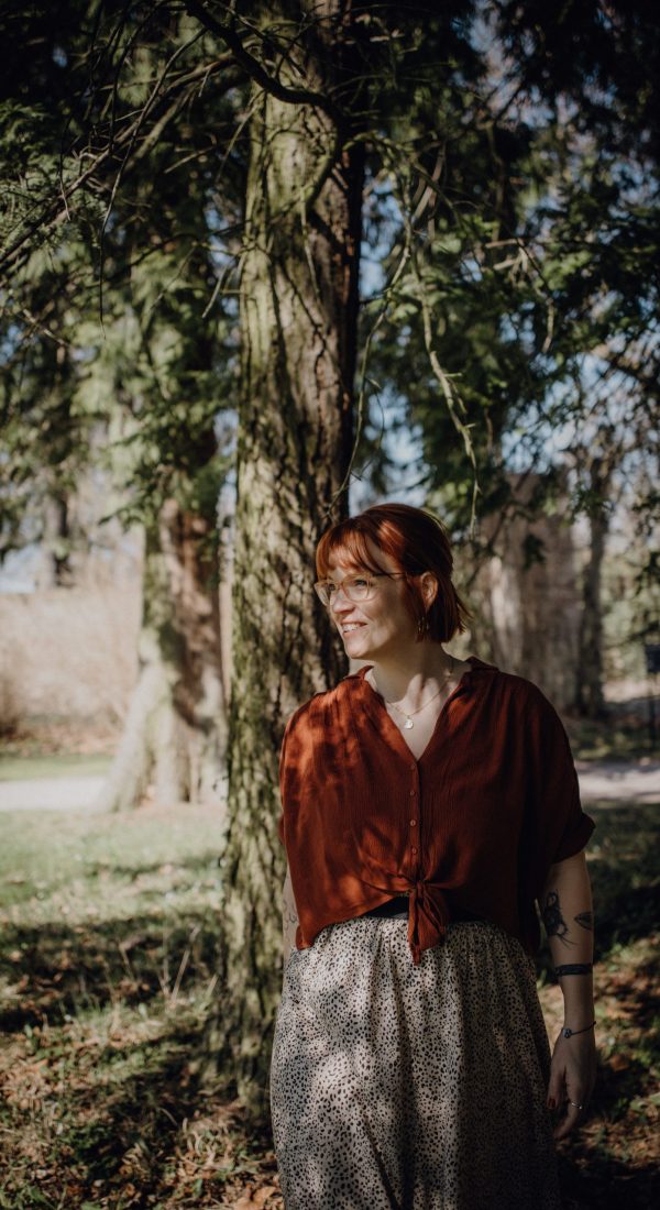 Karoline Krey, Coachin für persönliche Transformation bei marvelousme, steht lächelnd im Sonnenschein unter Bäumen in einem Park